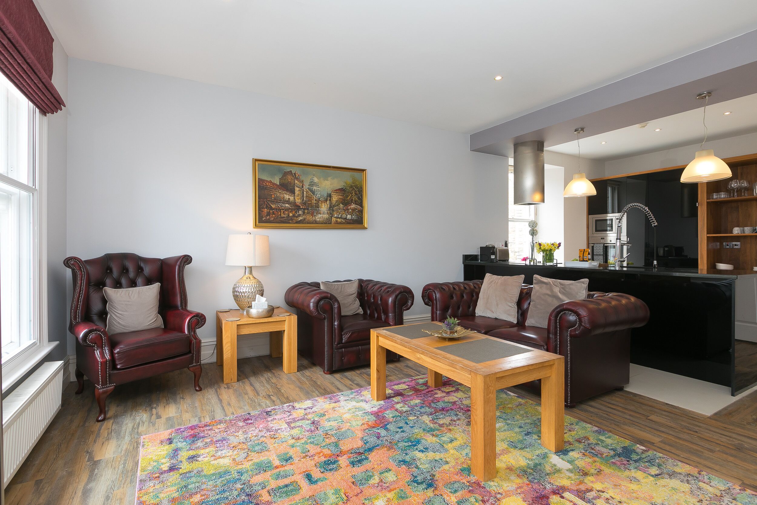 A living room with a fireplace, leather armchairs, a wooden coffee table, and a colorful rug.