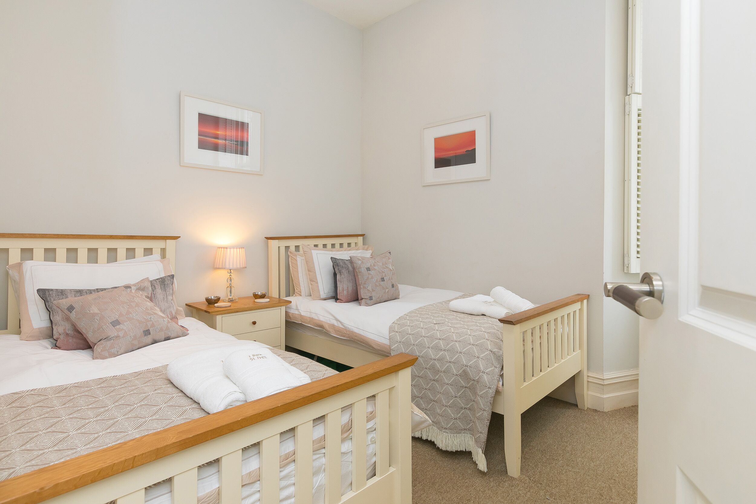 A bedroom with two beds, a nightstand with a lamp, and two framed pictures on the wall.