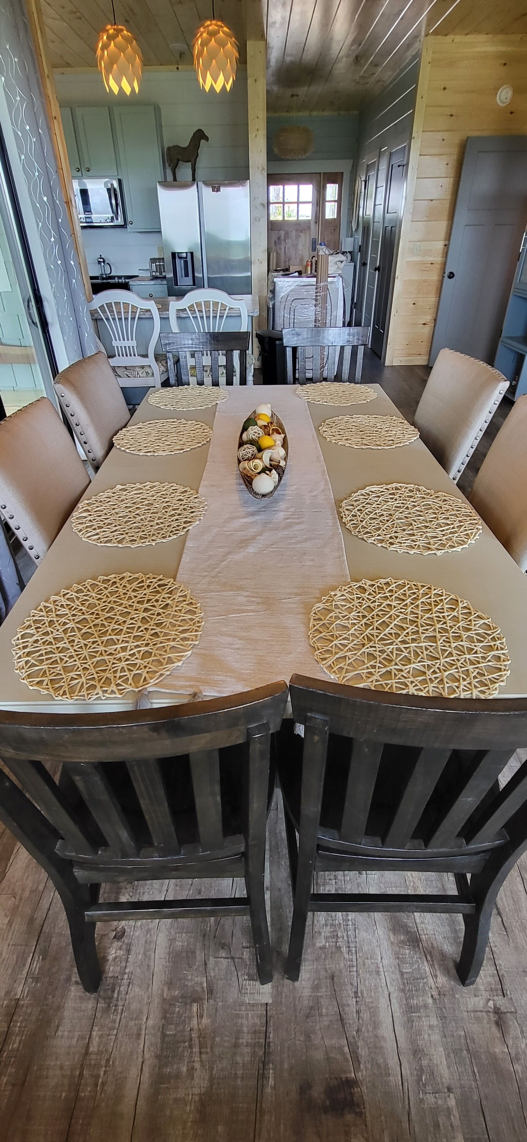Un coin repas avec une longue table en bois, six chaises et un grand saladier à fruits placé au centre.