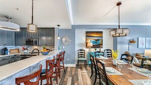 A modern kitchen with a central island, bar stools, and a dining area with a wooden table and chairs.
