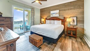 A bedroom with a large bed, wooden panel walls, a ceiling fan, and a view through a glass door to an outdoor area.