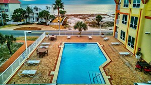 A pool area with lounge chairs and a view of the beach.