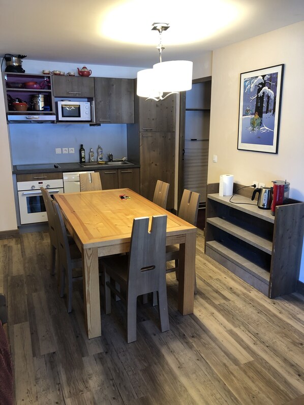 A modern kitchen with wooden cabinets, a built-in oven, microwave, and a dining area with a wooden table and chairs.