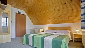 Una camera da letto con un soffitto in legno spiovente, un letto con copripiumino verde e bianco, un comodino con una lampada e una porta con il cartello di uscita.