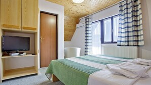 A bedroom with a bed, a TV on a shelf, a chair, and a window with curtains.
