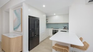 Una cocina moderna con armarios blancos, un refrigerador negro, una isla blanca y taburetes de mimbre.