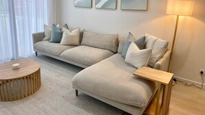 Una sala de estar moderna con un sofá seccional color crema, una mesa de centro redonda de madera y una lámpara de pie.