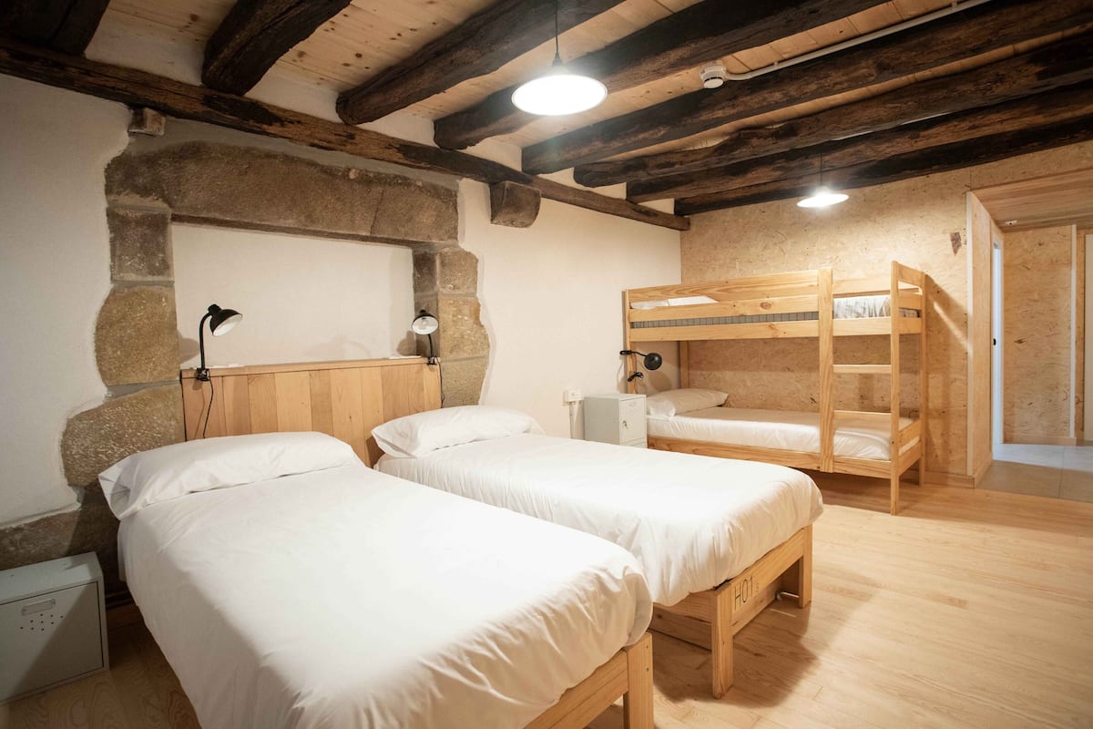 A room with two single beds, a bunk bed, a stone wall, and a wooden ceiling.