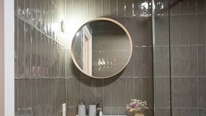 A bathroom with a round mirror, a white sink, and a small vase with flowers. - Paorra Baserria (Aia)