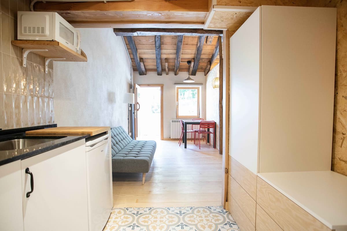 A compact kitchen with a microwave, a wooden ceiling, a sofa, and a dining area with a table and chairs.