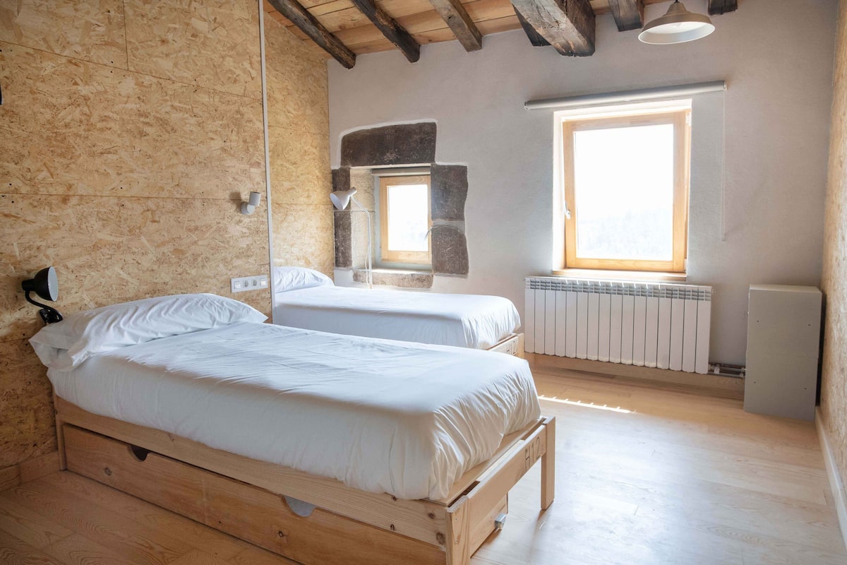 A bedroom with two wooden beds, a stone wall, a window, and a radiator.