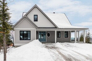 A modern two-story house with a covered porch, large windows, and a snow-covered landscape.