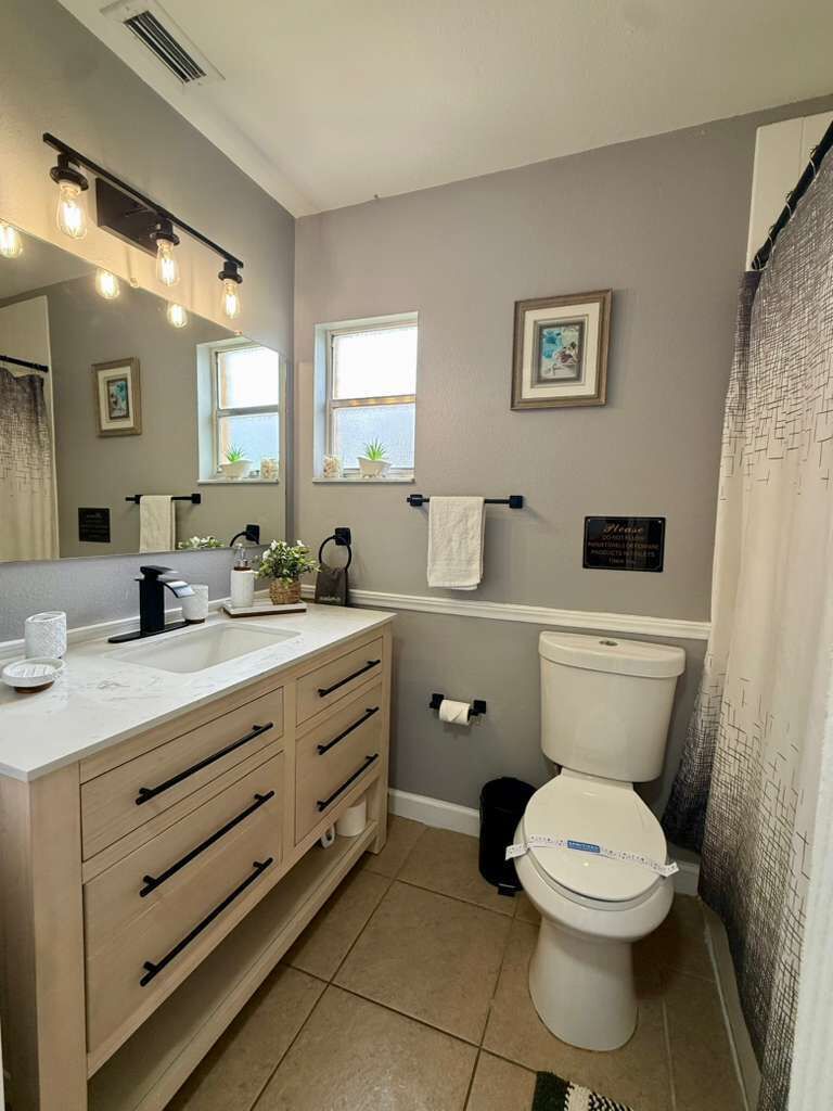 A bathroom with a sink, mirror, toilet, and shower curtain.