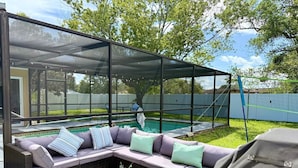 A covered outdoor seating area with a pool, a glass coffee table, and a grill. - Entire home with Screened- In Pool , Fully Fenced. (Spring Hill)