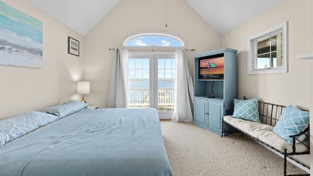Een slaapkamer met een bed, een televisie, een bank en een raam met gordijnen.