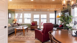 A spacious living room with a wooden ceiling, a dining table, and a view of a lake through large windows. - MINNeSTAY* Water's Edge Retreat (Waverly)