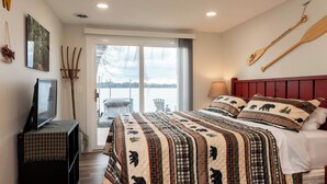 A bedroom with a large bed, a television on a stand, a window with a view of a body of water, and a wooden paddle on the wall. - MINNeSTAY* Water's Edge Retreat (Waverly)