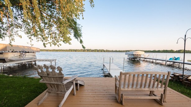 A wooden deck with two Adirondack chairs facing a lake, docked boats, and a clear sky. - MINNeSTAY* Water's Edge Retreat (Waverly)