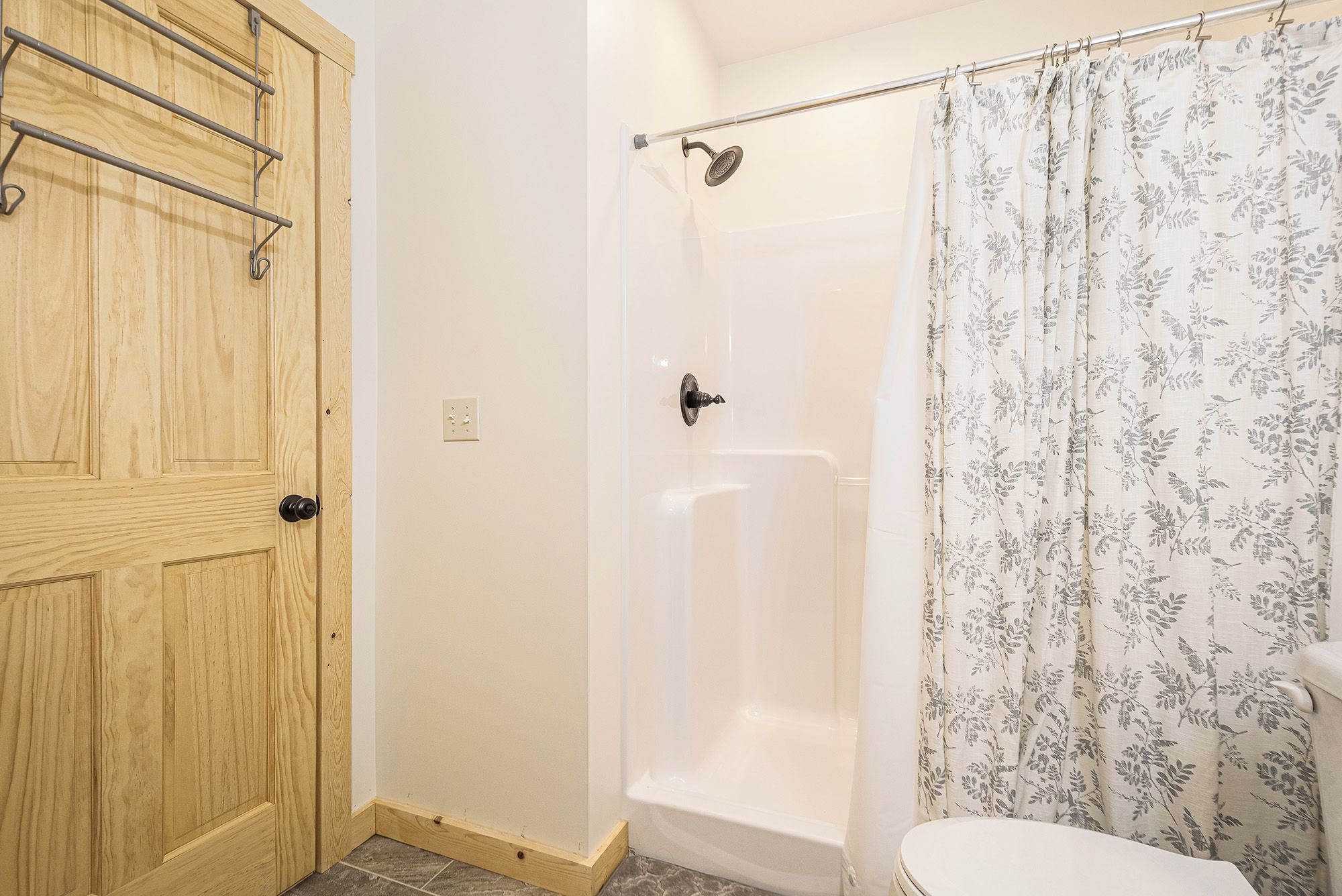 A bathroom with a wooden door, a shower with a floral curtain, and a white bathtub.