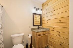 Un baño con inodoro, tocador de madera, encimera de granito y espejo.