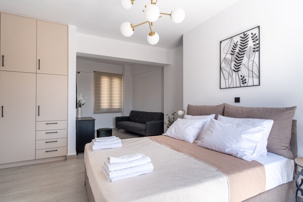 A modern bedroom with a large bed, a wardrobe, a sofa, and a wall-mounted artwork.