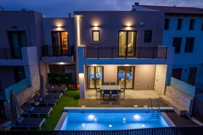 A modern two-story building with a swimming pool, outdoor seating, and a balcony.