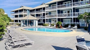 Un hotel de varios pisos con una zona de piscina, que incluye sillas de descanso y un pabellón.