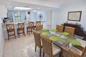 A dining area with a glass table, wicker chairs, and a kitchen in the background.