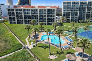 A hotel with a swimming pool surrounded by palm trees and lounge chairs.