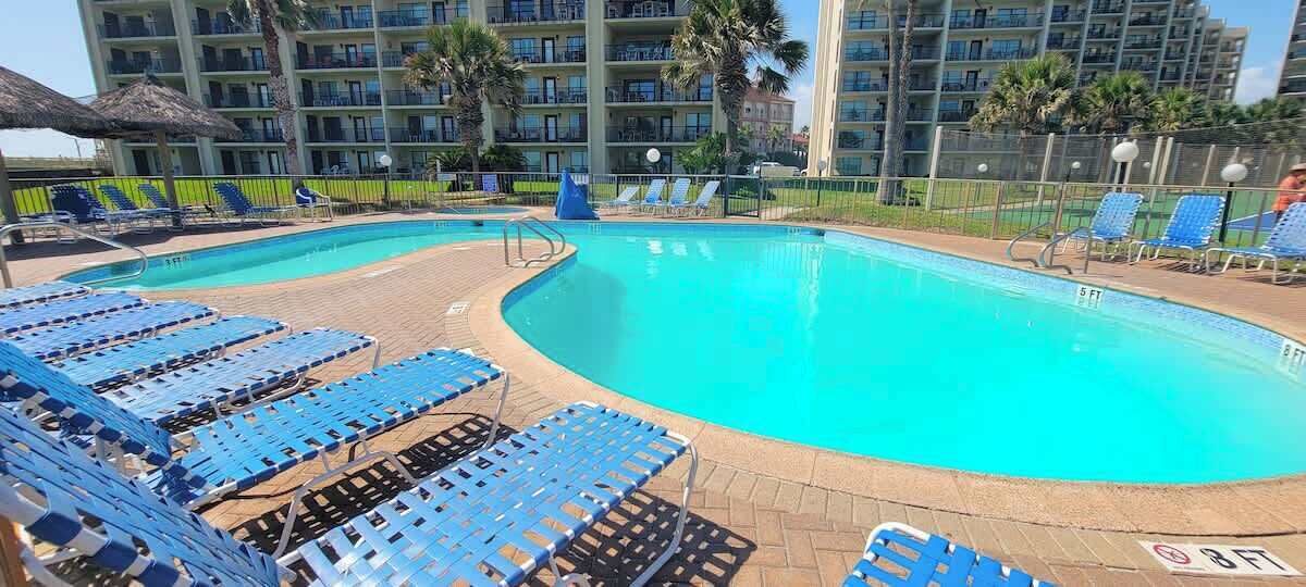 A swimming pool with blue lounge chairs and a fenced area.