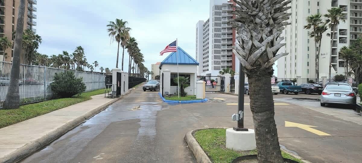 A street with a small blue kiosk, palm trees, and tall buildings.