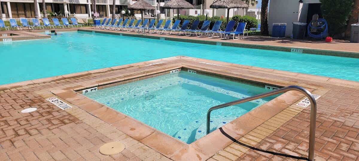 Een zwembad met een jacuzzi, ligbedden en een terras van baksteen.