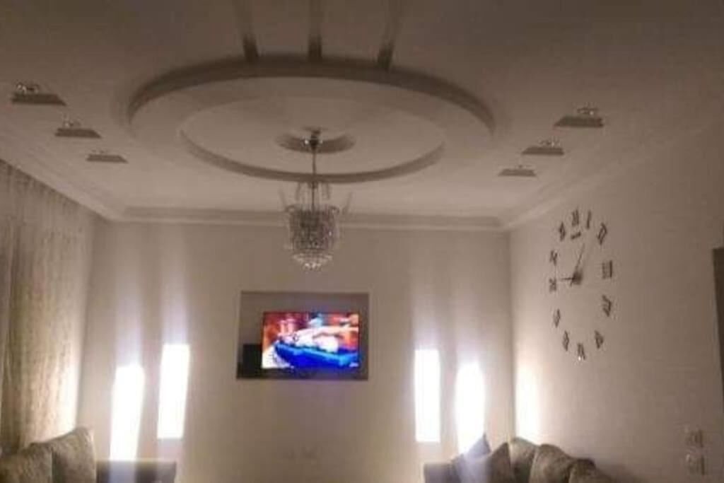 Ein Wohnzimmer mit Fernseher, einer Uhr und einer Kristallleuchter.