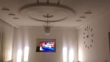 A living room with a television, a clock, and a chandelier.