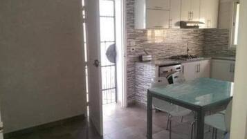 Une cuisine avec des meubles blancs, une table en verre et un mur recouvert de carreaux.