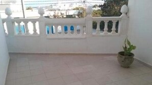 Een balkon met een witte reling, een bloempot en een betegelde vloer.
