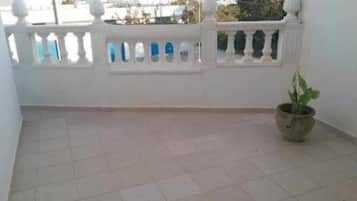 A balcony with a white railing, a potted plant, and a tiled floor.