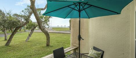 Un patio al aire libre con una mesa y sillas, una sombrilla verde y vistas al mar.