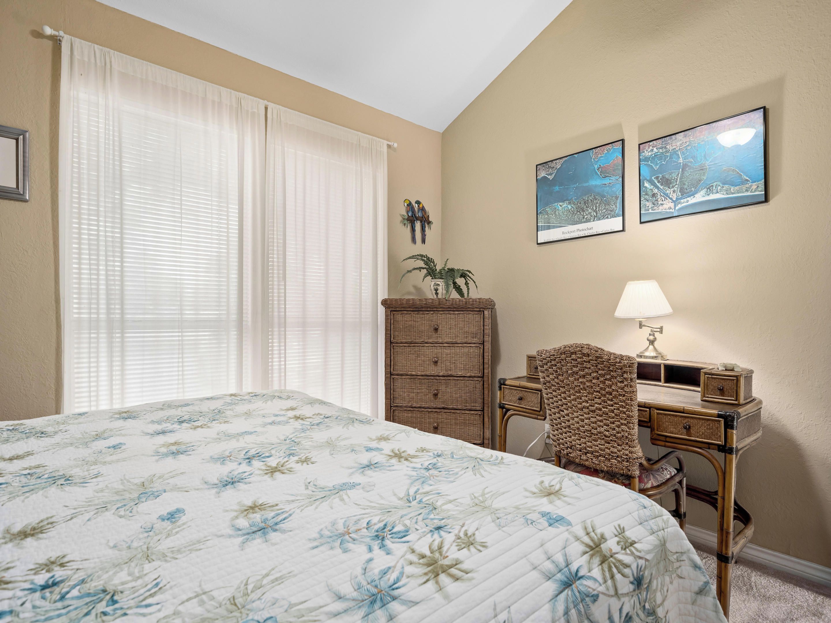 A bedroom with a large bed, a desk with a lamp, and two framed photos on the wall.