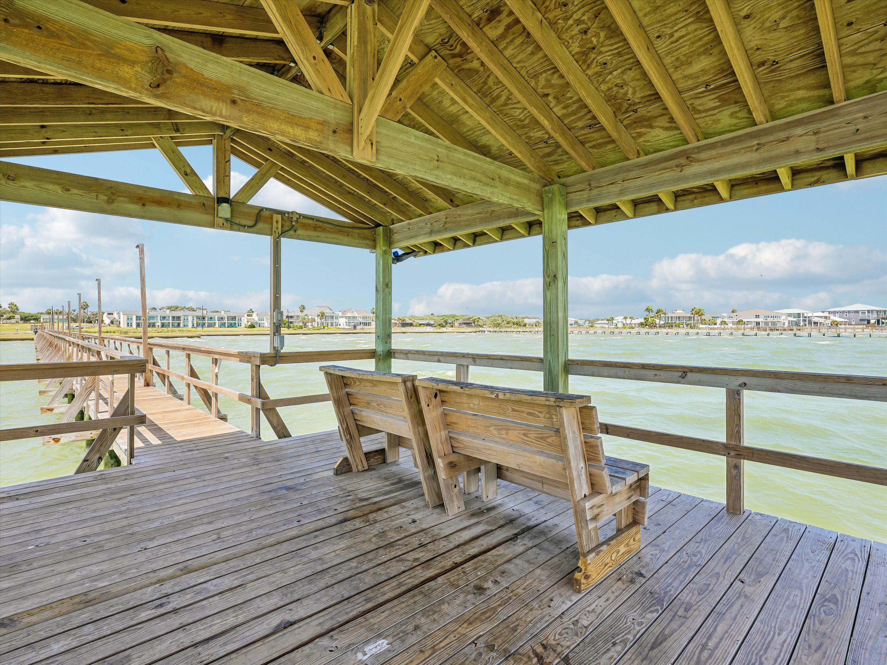 Eine hölzerne Pier mit Bänken, einem überdachten Bereich und Blick auf das Wasser sowie Gebäude in der Ferne.