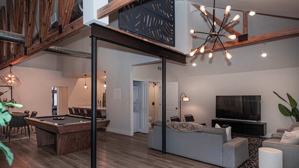 Een moderne woonkamer met een pooltafel, grijze banken, een televisie en een bijzondere plafondlamp.