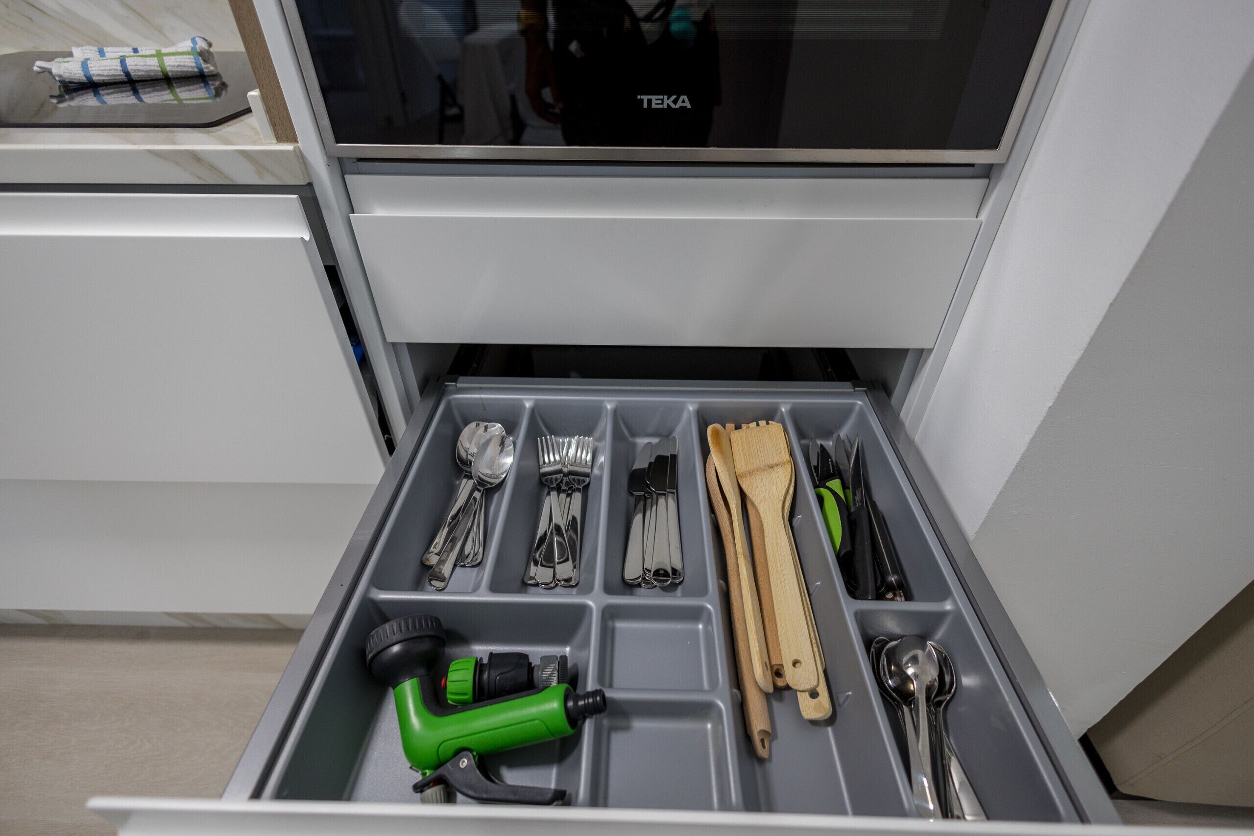 Un tiroir compartimenté contenant divers ustensiles, un outil électrique vert et une brosse en bois.