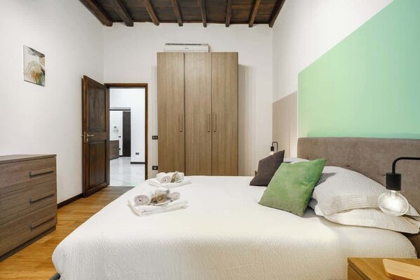 Un dormitorio con una cama grande, un armario, una mesita de noche y una mesita auxiliar.