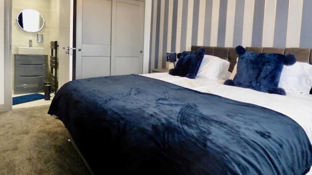 A bedroom with a large bed, a dresser, a mirror, and a striped wall. - blackpools (Thornton Cleveleys, Blackpool)