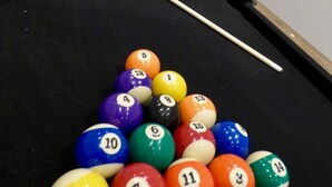 A pool table with balls arranged in a triangle formation, a cue stick, and a white wall in the background. - blackpools (Thornton Cleveleys, Blackpool)