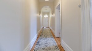 A hallway with a patterned rug, white walls, and a door at the end.
