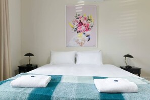 Et hotelværelse med en seng, to sengeborde, et blomsterbillede og et blåt og hvidt ternet tæppe.