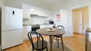 A compact kitchen with white cabinets, a round wooden table, and two chairs.
