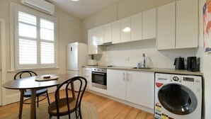 A compact kitchen with white cabinets, a built-in oven, a washing machine, and a dining area with a table and chairs.