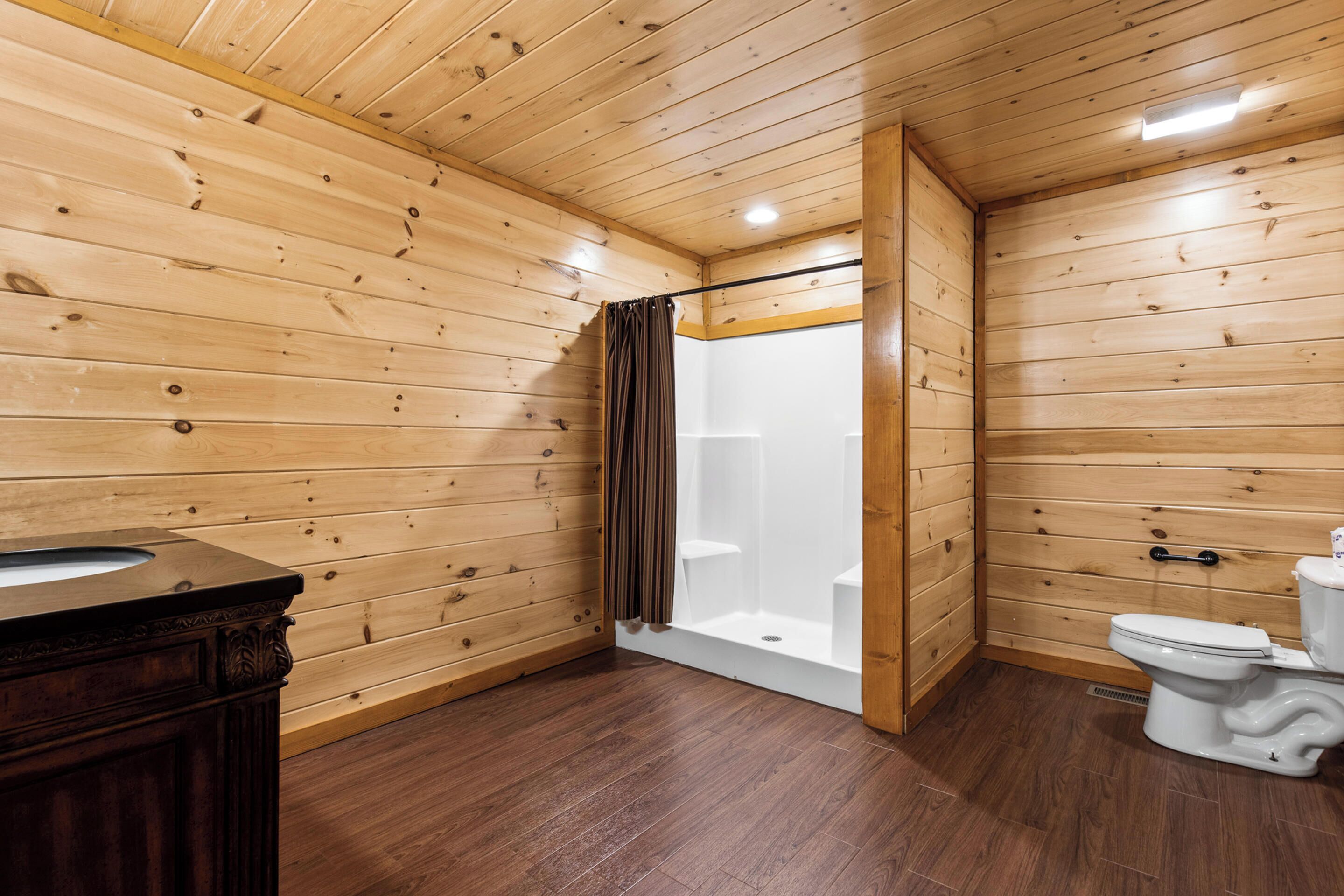 A wooden-paneled bathroom with a shower, toilet, and vanity.